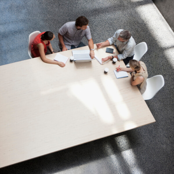a group of people sitting around a table with a laptop and papers